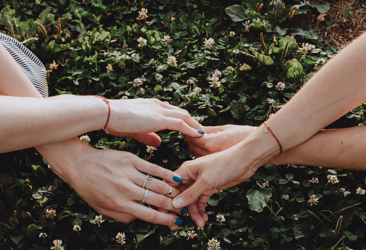 Mains de femmes reliees par un fil de laine bleu lors d'un rituel de deconnexion collective.